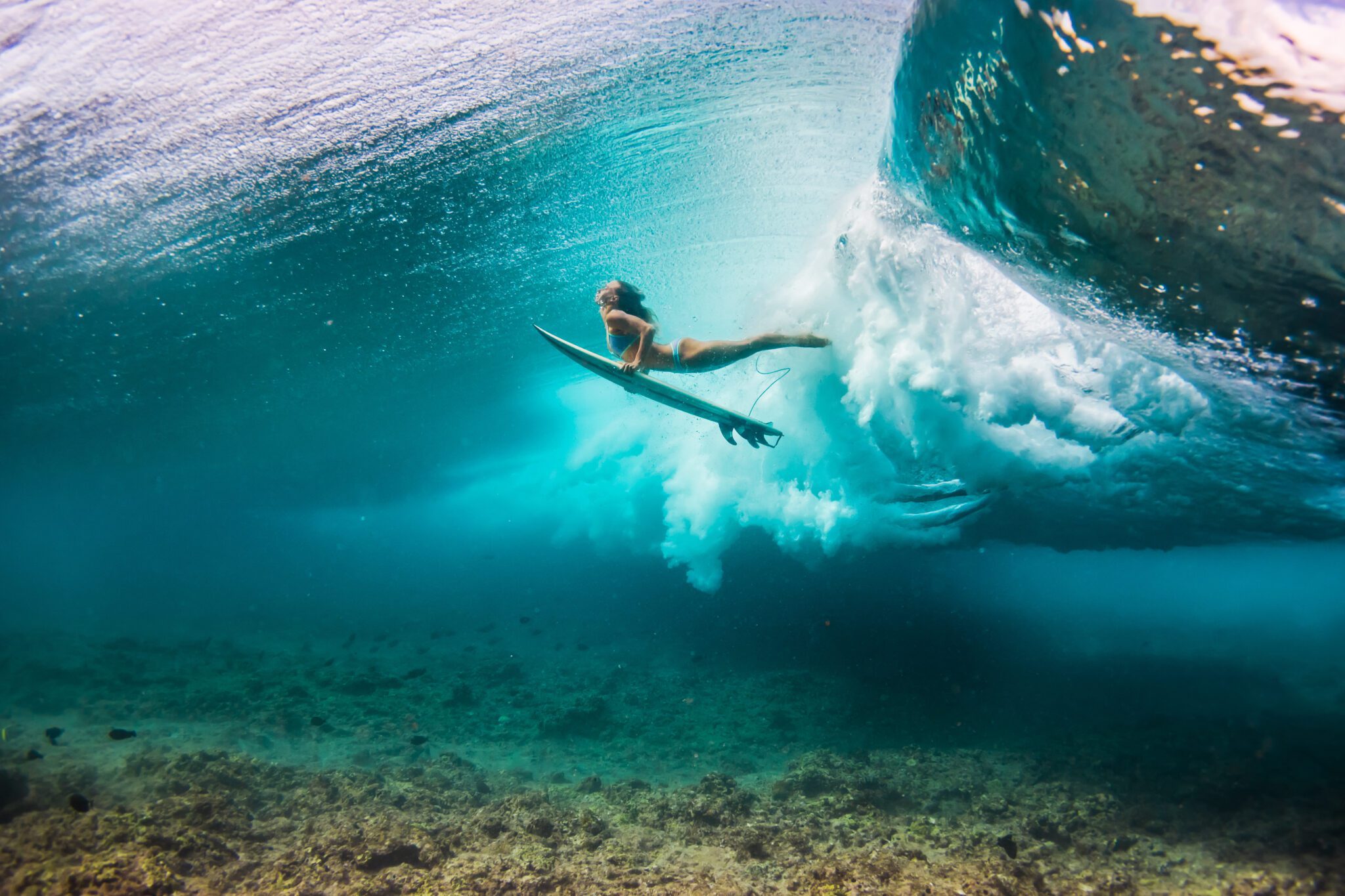 woman in bikini doing duck dive with the surfboard under the wav